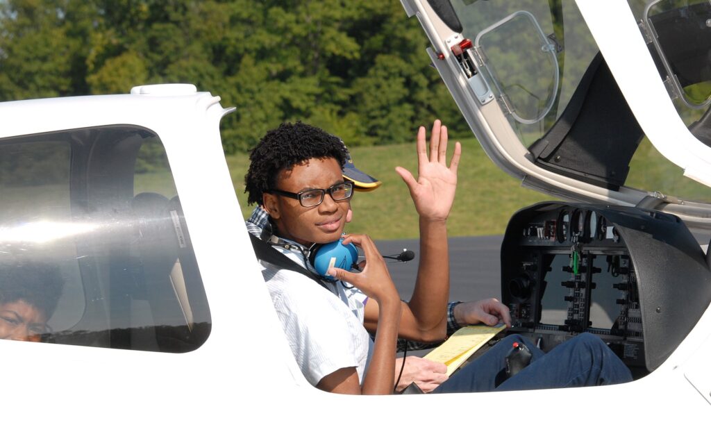 Young Black teenager waving goodbye as he is getting ready to fly an airplane